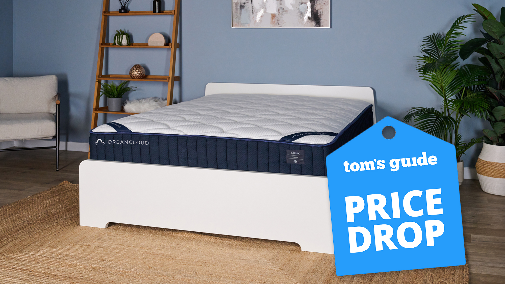 The DreamCloud Classic Hybrid Mattress on a white wooden bedframe in our blue sleep lab, with a blue Tom&#039;s Guide price drop badge overlaid on the bottom right hand corner