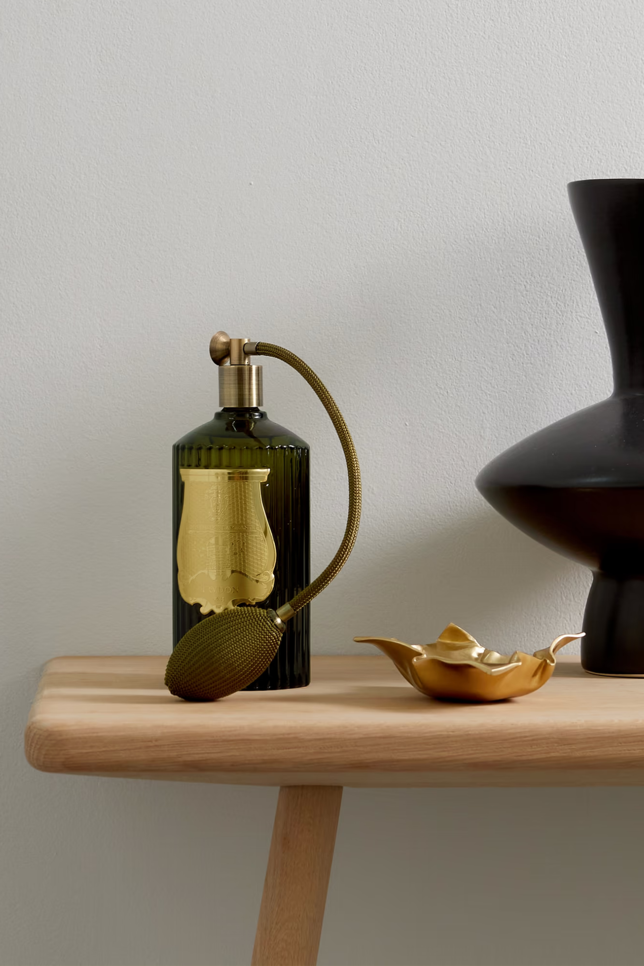 A green glass room spray on a side table with a gold bowl