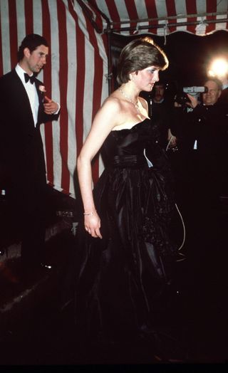 Princess Diana wearing a black strapless gown standing next to Prince Charles wearing a tuxedo on a staircase in 1981