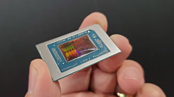A close-up of an AMD Ryzen APU held between two fingers, showing the chip’s reflective die surface and intricate packaging details.