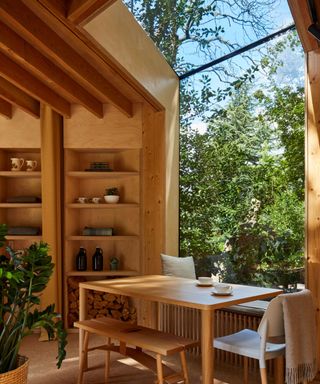 A wooden lake house with a full-wall window, a dining table and built-in shelving on the walls