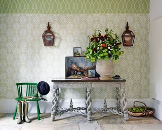 An entry table decor idea with grey table, green wallpaper, flowers and paintings of pheasants