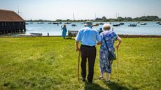 an elderly man and woman walk arm in arm and with canes towards a harbor full of sailboats