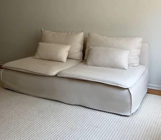 Image of a plain, beige sofa in a living room that has white walls and a white rug