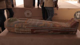A painted human-shaped sarcophagus on a table under a tent.