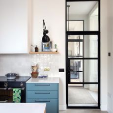 white kitchen with oven and blue drawers next to black framed door