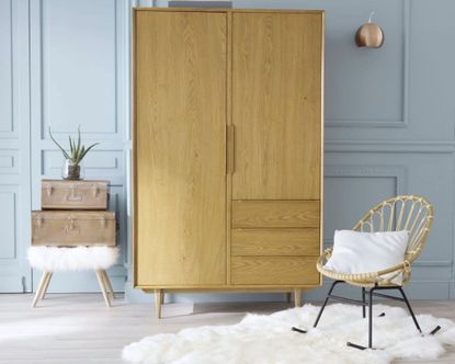 Rattan rocking bedroom chair in blue bedroom beside wardrobe and atop white sheepskin rug