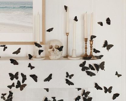 在壁炉架上DIY万圣节装饰，使用黑色蝴蝶，白色蜡烛和头骨