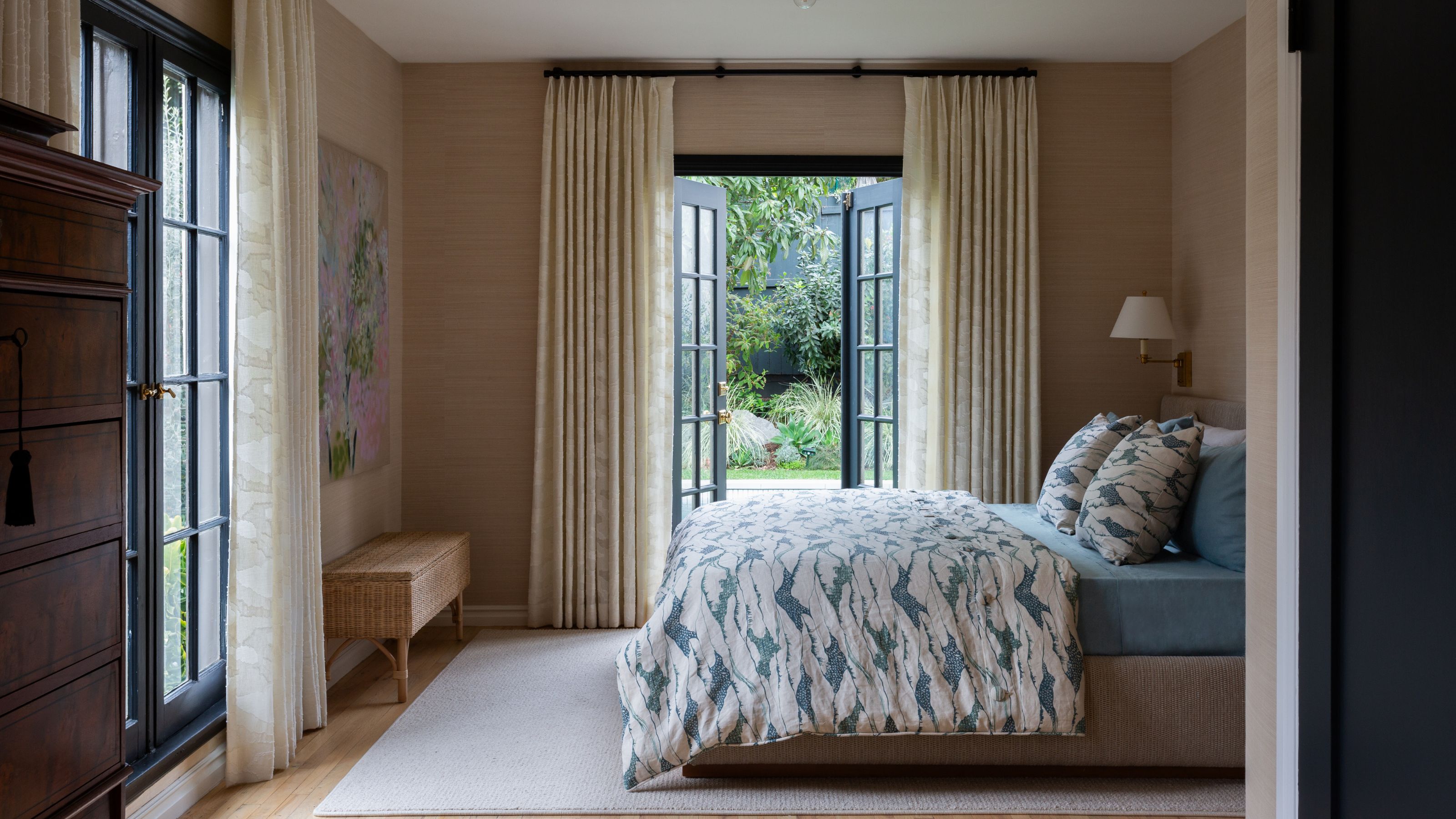 a large primary bedroom with soft beige grasscloth wallpapered walls and two sets of french patio doors