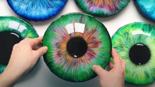 A shot of an artist's hand with an array of acrylic eye paintings
