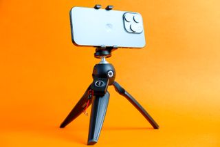 A photo of the Joby HandyPod Mobile Plus holding an iPhone 15 Pro against an orange background