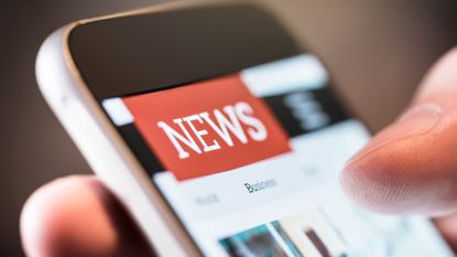 A person holding a smartphone in their hand looking at the news