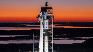 A white and black rocket on the launch pad at sunrise for Crew-10