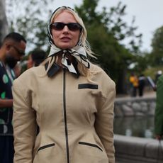 A Guest is seen wearing a beige barn jacket with a silk head scarf at the MKDT Studio show. 