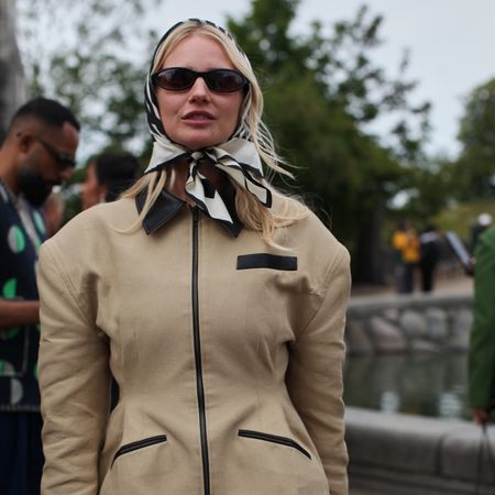 A Guest is seen wearing a beige barn jacket with a silk head scarf at the MKDT Studio show. 