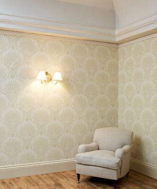 neutral living room corner with beige patterned wallpaper, wall light and traditional armchair