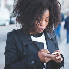 Woman in black trench coat texting