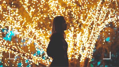 Woman alone walking in front of tree brightly lit in lights at Christmas, to represent feeling lonely at Christmas