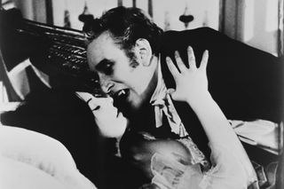 Black and white photo of a vampire about to bite a woman's neck in an old movie.