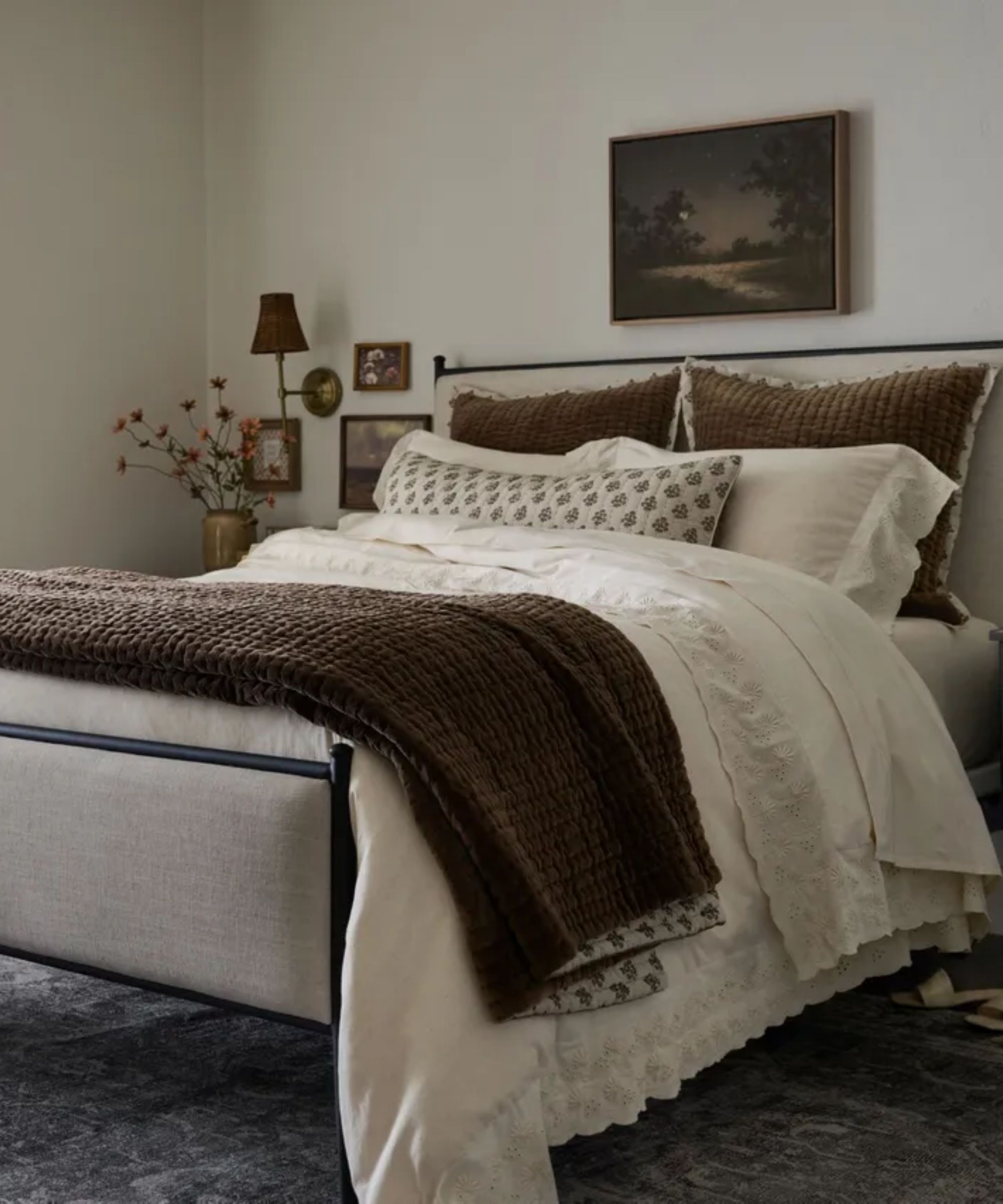 bedroom styled for the magnolia fall collection with an iron and upholstered linen bed styled with white broderie anglaise linens and block print floral and velvet accent pillows and throws