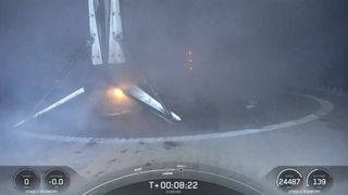 A black and white spacex falcon 9 rocket first stage sits on the deck of a ship at sea.