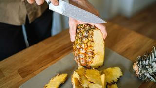 Hands chopping pineapple on board