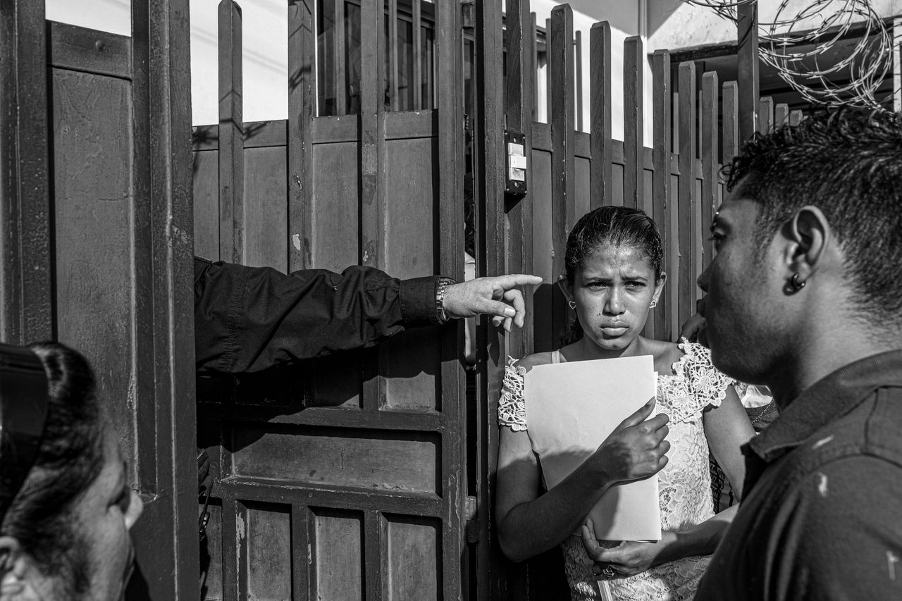 Asylum seekers wait at the gates of the Mexican Commission for Aid to Refugees (COMAR) for an asylum hearing. Tapachula, Mexico 2019. From the series &ldquo;The Two Walls&rdquo;