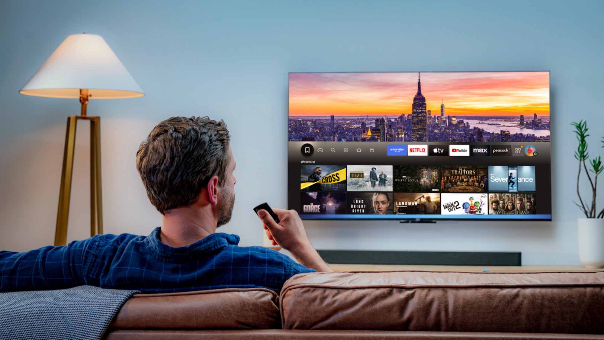 A man in a blue shirt sitting on a couch watching Amazon Fire TV on a TV on the wall. 