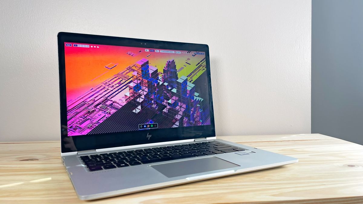 An HP EliteBook x360 1030 G2 running Fedora Linux on a wood table with the lid open