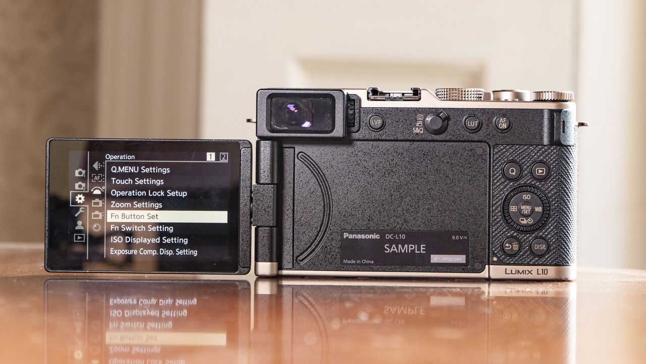 Rear of the Titanium Gold special edition of the Panasonic Lumix L10 compact camera, with the screen flipped out, on an antique wooden table