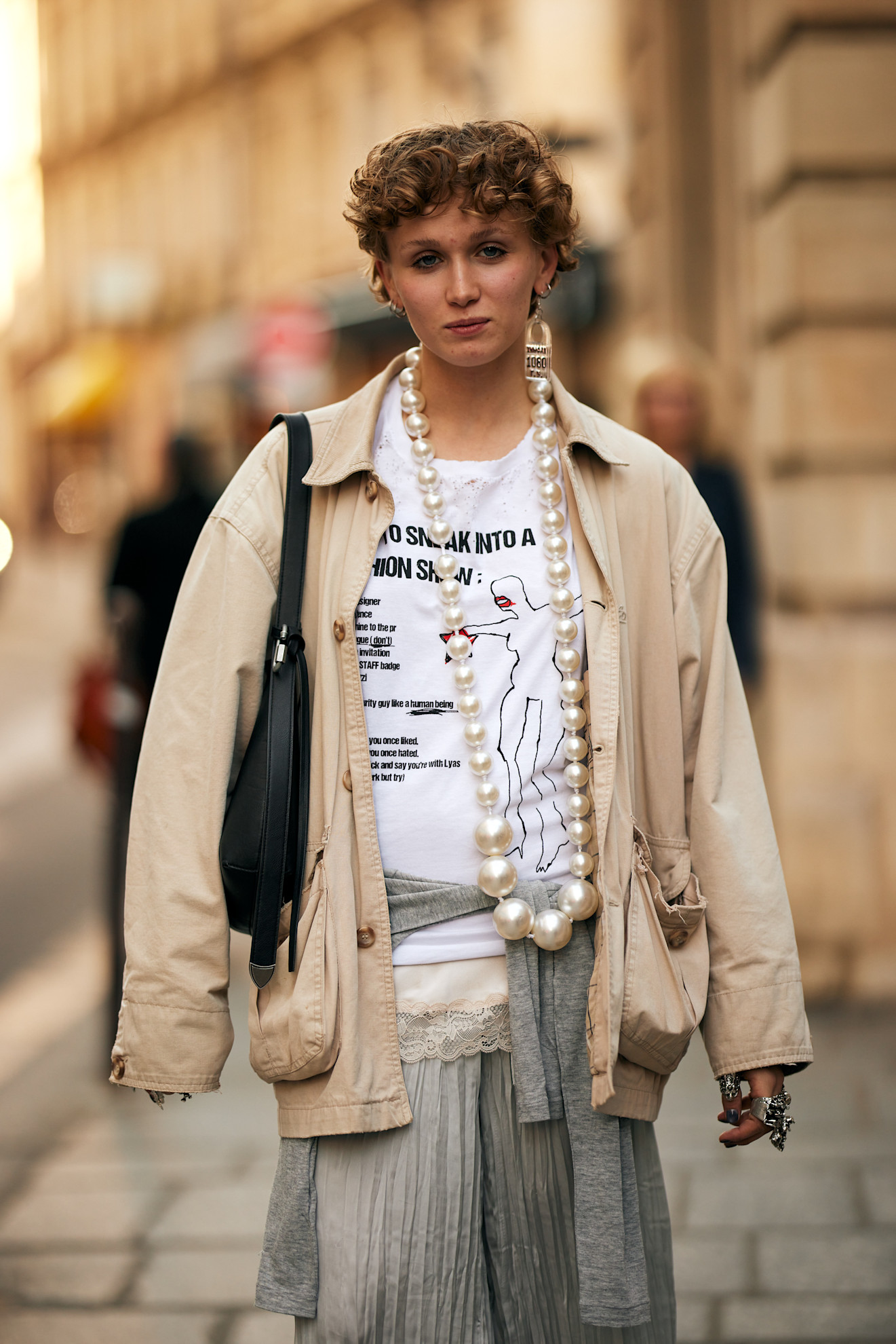 a woman with a short pixie cut wearing a cream bomber jacket, white t-shirt, and a large strand a pearls