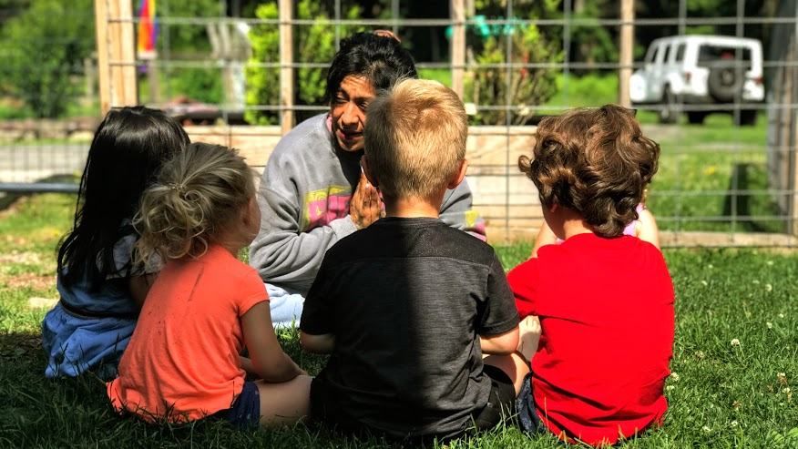 A woman smiles at a circle of children