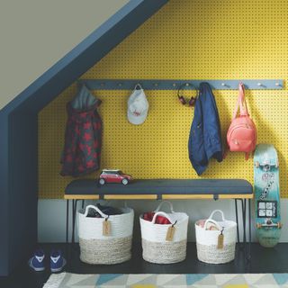 Understairs nook with yellow pegboard wall and bench over storage baskets
