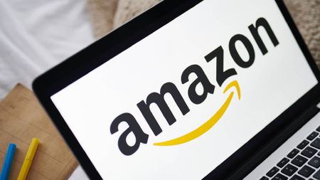 Amazon logo on laptop next to blue and yellow pens.