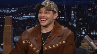 Pete Davidson sits laughing in front of a New York backdrop in The Tonight Show with Jimmy Fallon.