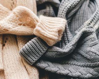 A beige cable knit sweater and a grey cable knit sweater with rolled sleeves