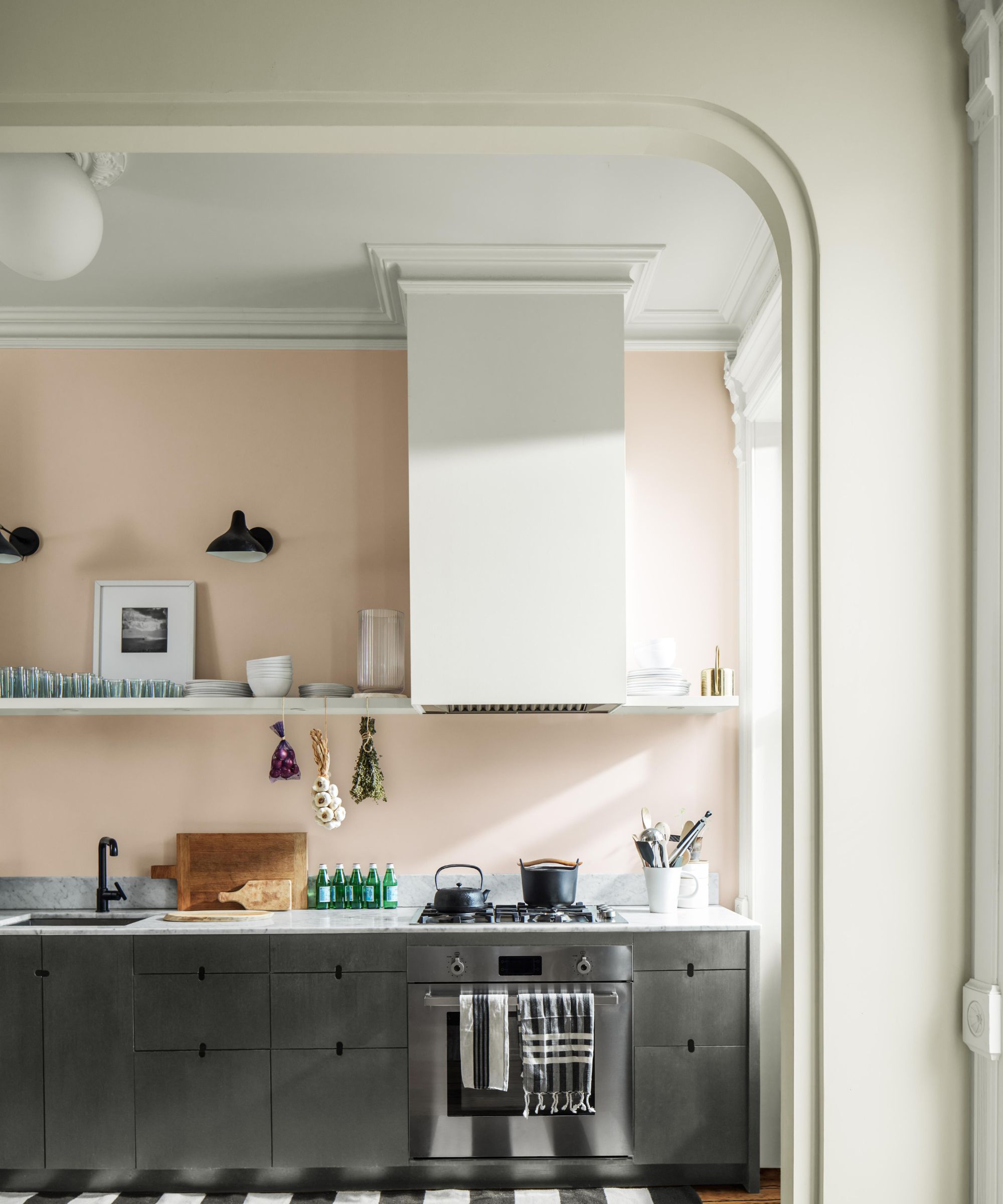 Curved doorway and molding entering into the kitchen with pastel pink wall, stainless steel cabinets, marble countertops