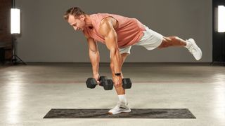 Man on exercise mat in studio performing a single leg Romanian deadlift with left leg raised and holding two dumbbells