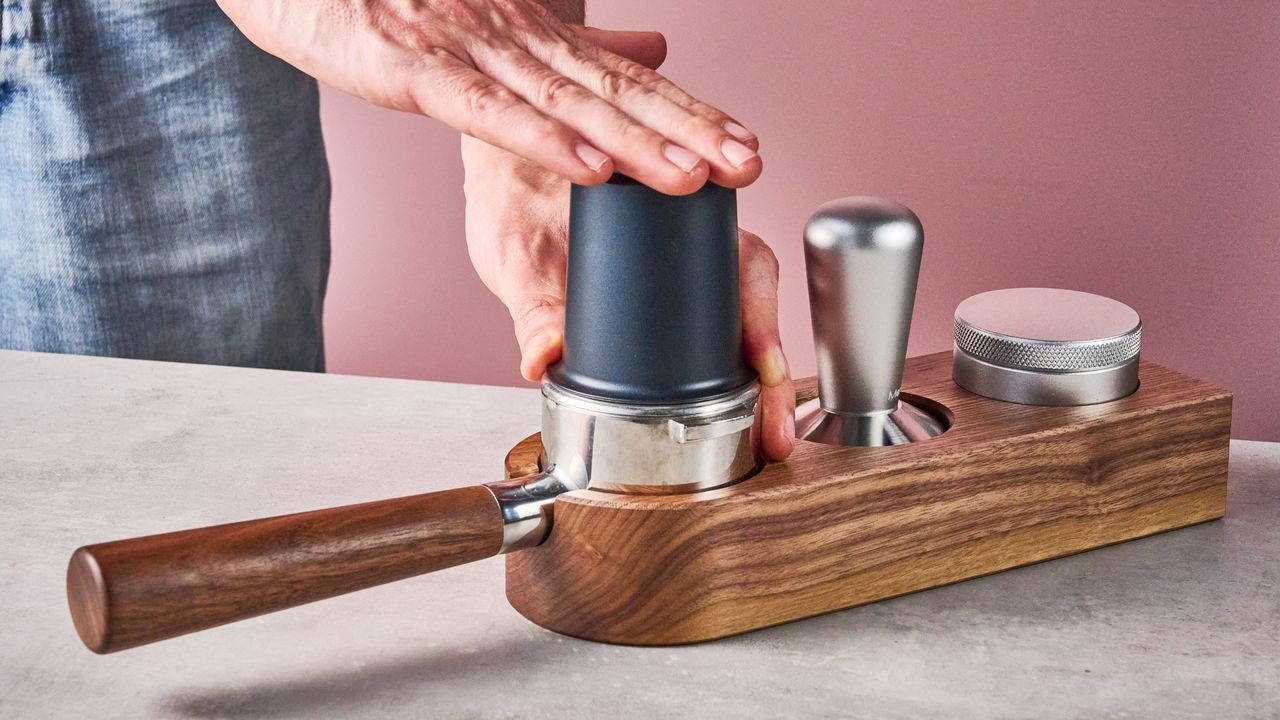 A man taps on top of the Meraki Espresso Machine's dosing cup, transferring the grounds into the portafilter.