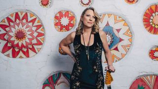 Susan Tedeschi with her guitar standing against a wall adorned with a mural of flowers 