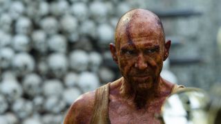 Ralph Fiennes stands slightly disturbed in front of a bunch of skulls in 28 Years Later.