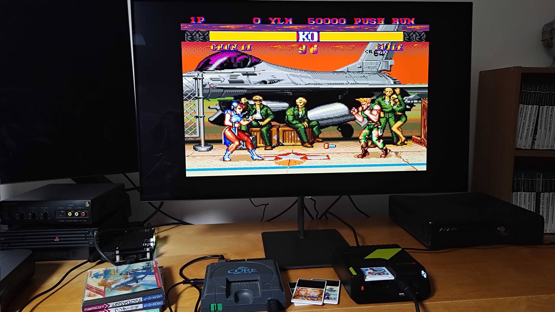 Hyperkin Retron GX next to PC Engine running Street Fighter 2 beneath monitor.