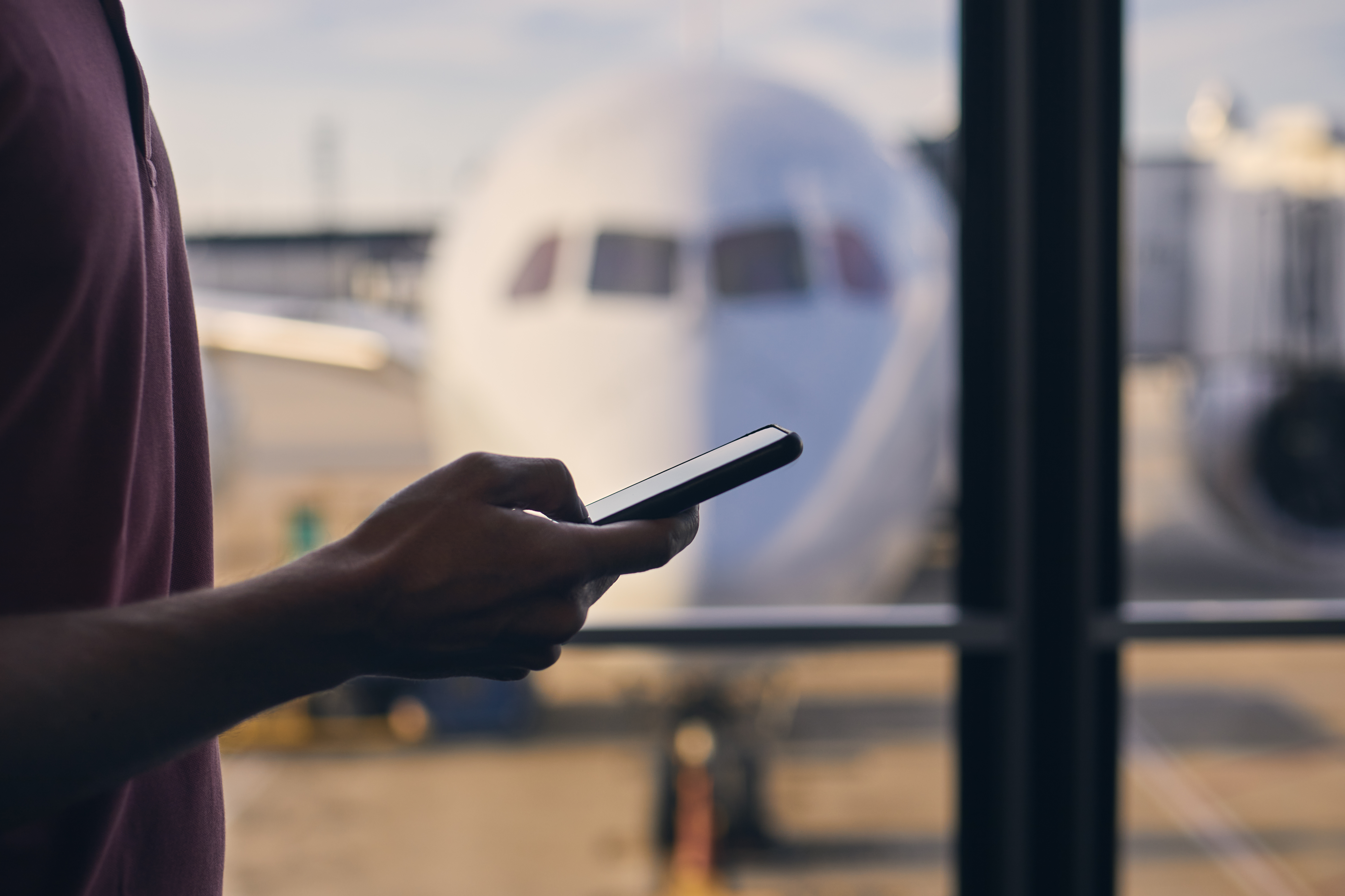 A man holds a smart phone in front of a window at an airport