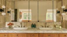 A beautiful bathroom with his and hers sinks, a stone counter, textured wood cabinets, glass mirrored cabinets, and a tiled backsplash
