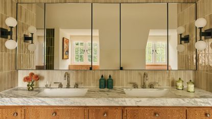 A beautiful bathroom with his and hers sinks, a stone counter, textured wood cabinets, glass mirrored cabinets, and a tiled backsplash