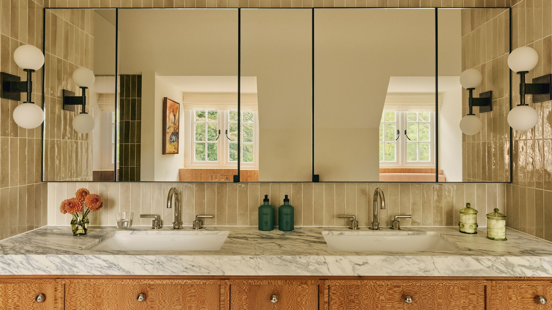 A beautiful bathroom with his and hers sinks, a stone counter, textured wood cabinets, glass mirrored cabinets, and a tiled backsplash