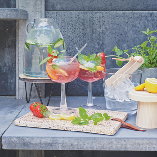 Outdoor cocktails, pink gin with strawberries in large glasses, chopping board with fresh mint. Summer drinks, alfresco.