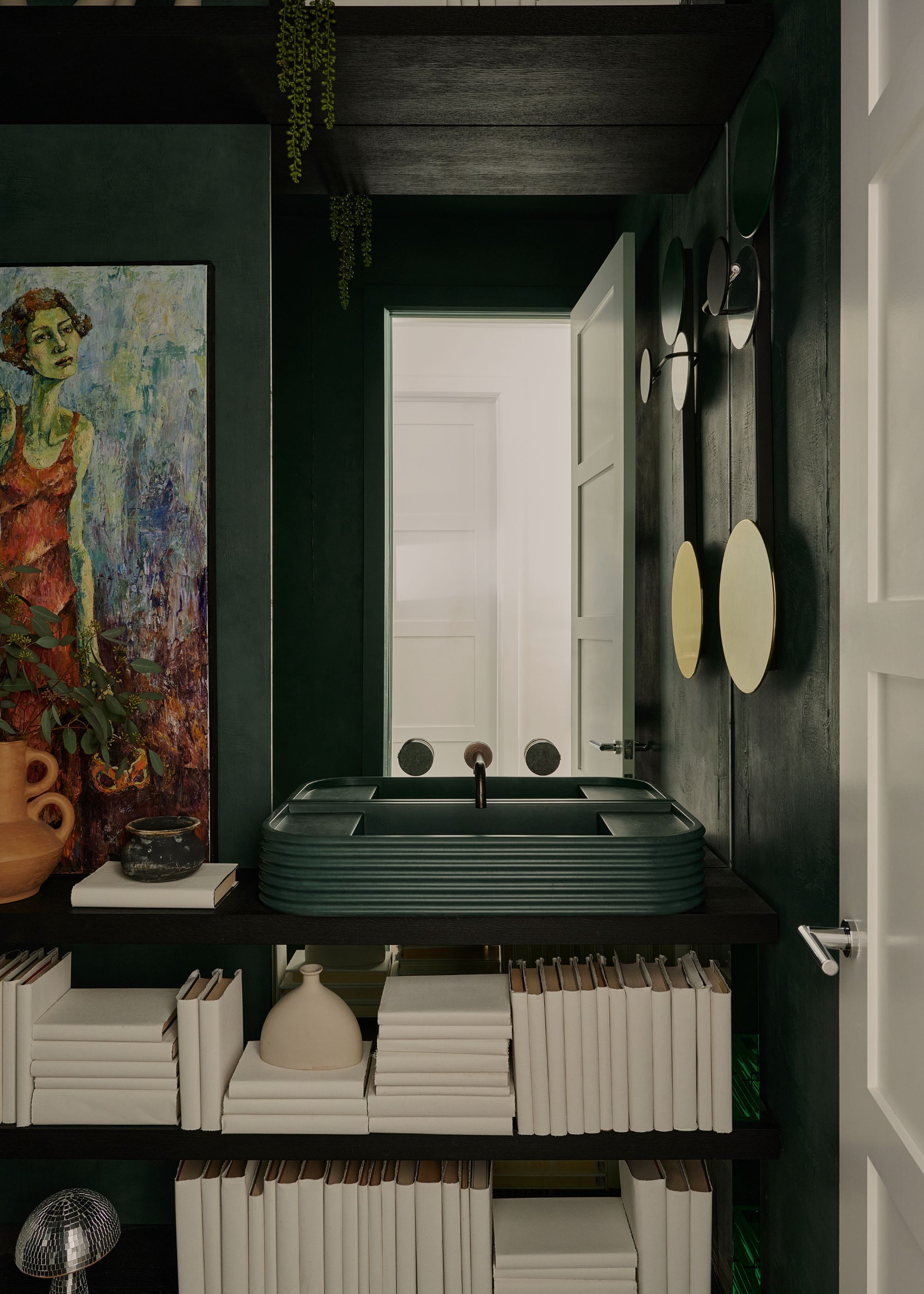 A powder bathroom with dark-painted walls, a vintage artwork and books covered in white paper