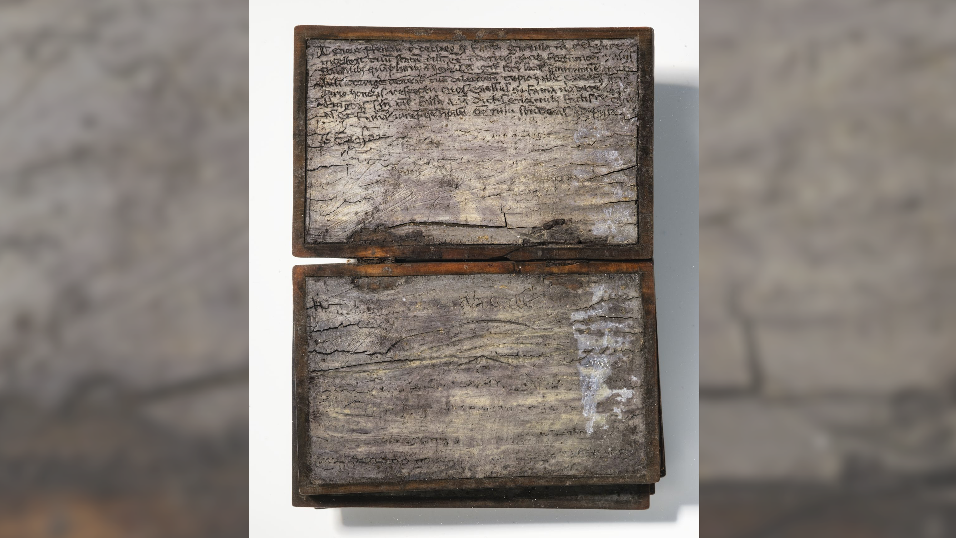 a small wooden notebook with wax pages that have been inscribed in cursive Latin