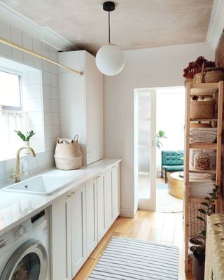 White utility room with white cabinets and brass fittings and wooden shelving